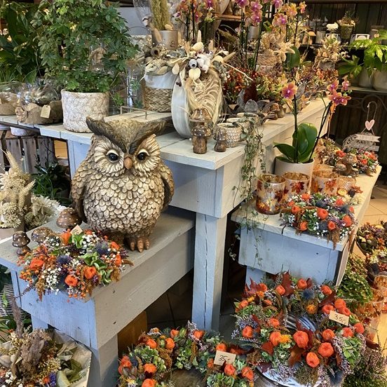 Dekorativer Verkaufsstand mit floralen Arrangements und einer Eule aus Keramik.