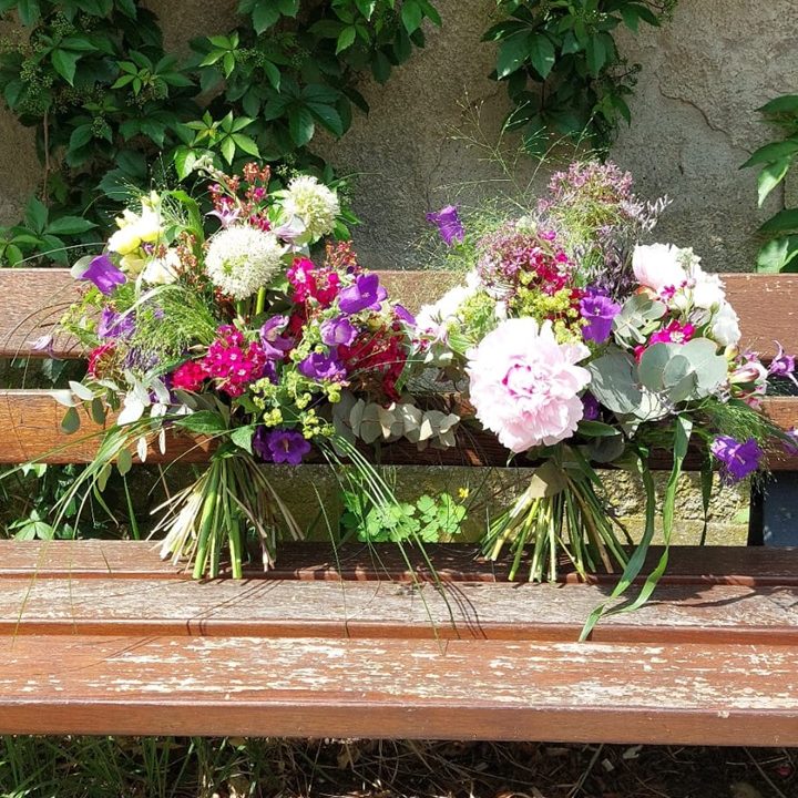 Zwei bunte Blumenarrangements auf einer Holzbank.