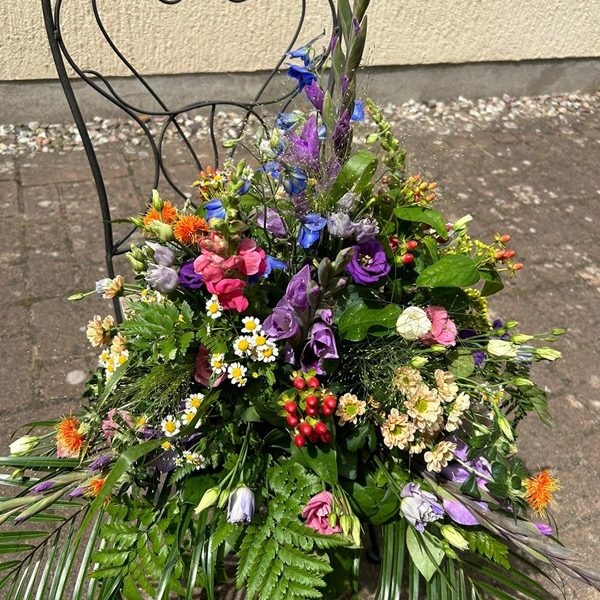 Bunte Blumenarrangement mit verschiedenen Pflanzen auf einem Metallstuhl.