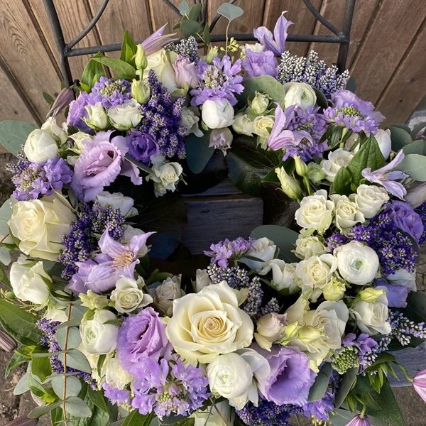 Bunter Blumenkranz mit lila, weißen und grünen Blumen, dekorativ angeordnet.