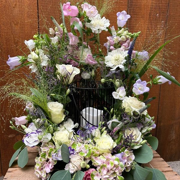 Bunte Blumenanordnung mit Rosen, Lisianthus und Gräsern in einem schwarzen Gitter.