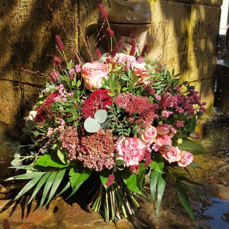 Bunter Strauß mit verschiedenen Blumen, darunter Rosen und grüne Blätter, am Wasserbecken.