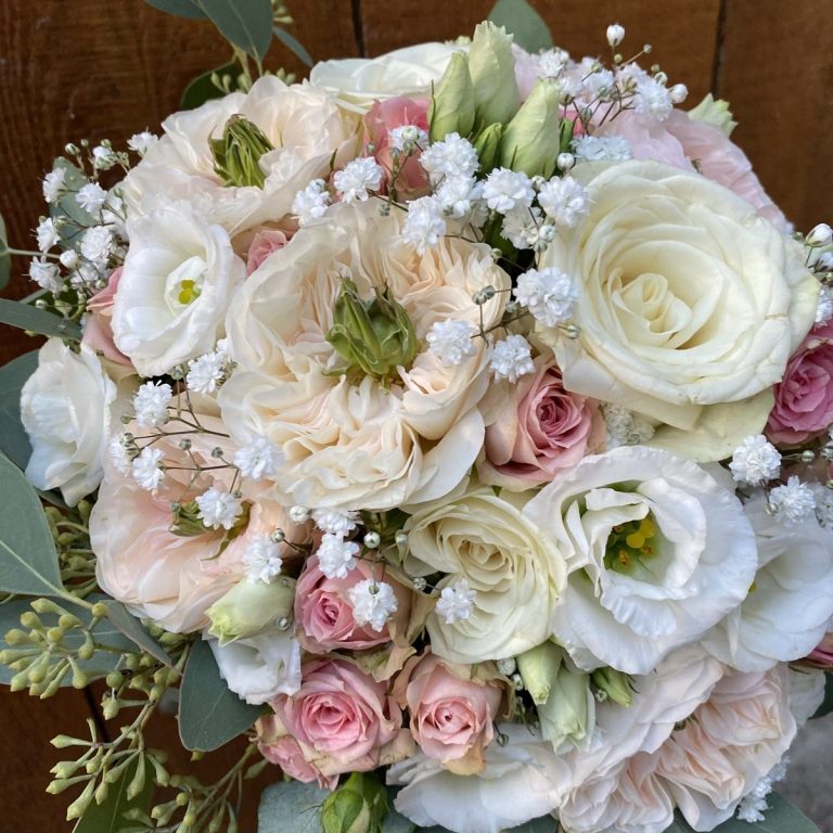 Bunte Blumenstrauß mit Rosen, Lisianthus und Schleierkraut vor Holzuntergrund.