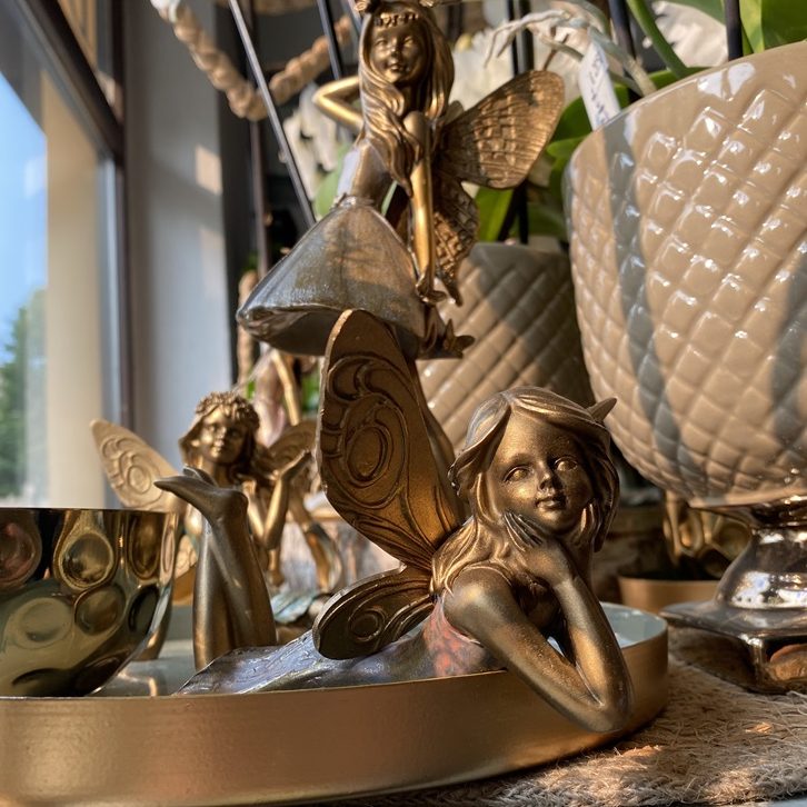 Goldene Feenfiguren und dekorative Töpfe auf einem Tisch neben einem Fenster.
